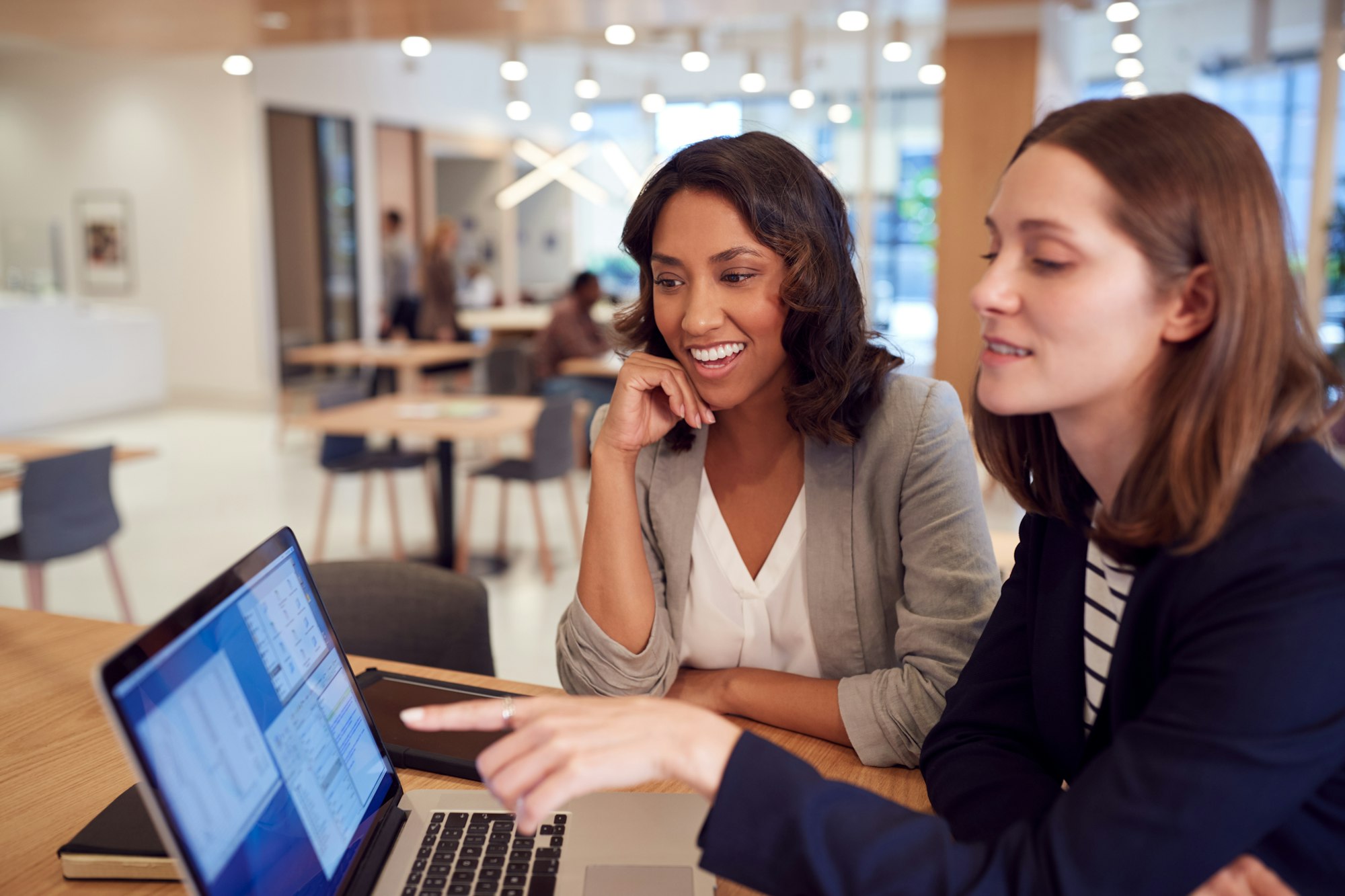 Two Businesswomen With Laptop At Desk In Open Plan Office Collaborating On Project Together